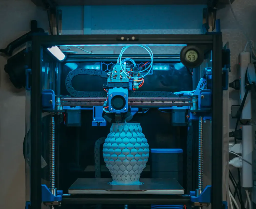 Une imprimante 3D fermée, éclairée en bleu, en train d'imprimer un vase
