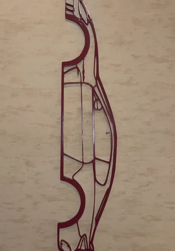 Silhouette filaire d'une voiture de sport imprimée en 3D en rouge sombre, accrochée à un mur clair