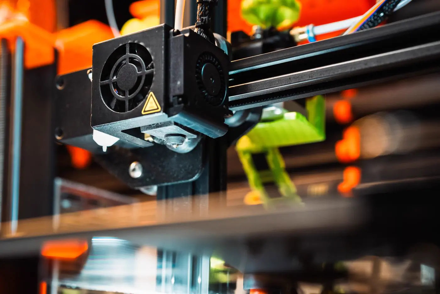 La tête d'une imprimante 3D à filament et son ventilateur, au-dessus du plateau, dans un atelier