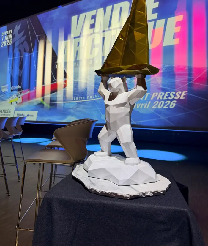Le trophée de la Vendée Arctique 2026, un ours blanc à facettes portant un voilier doré, posé sur une scène devant un grand écran